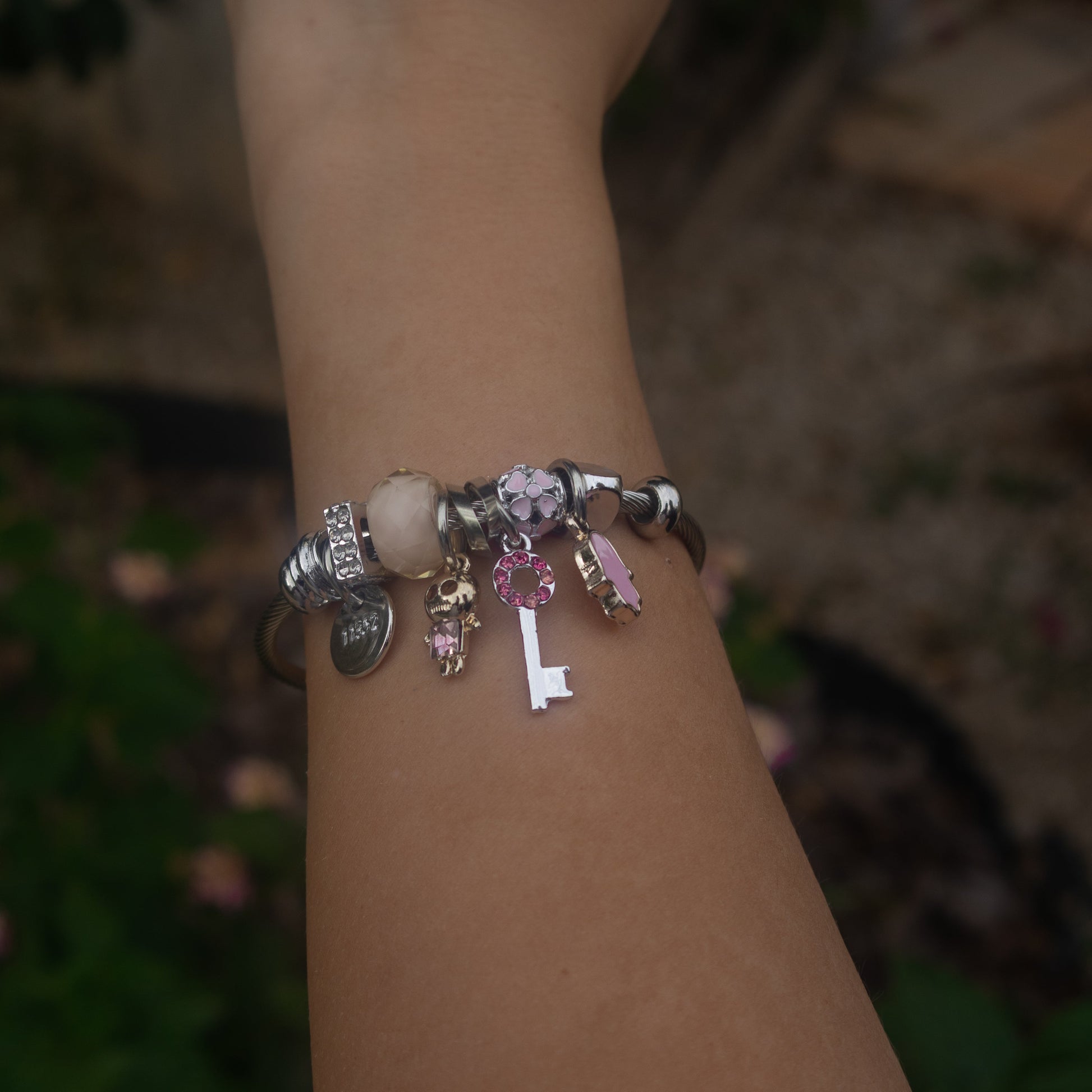 Hand wearing a bracelet with charms against a blurred natural background