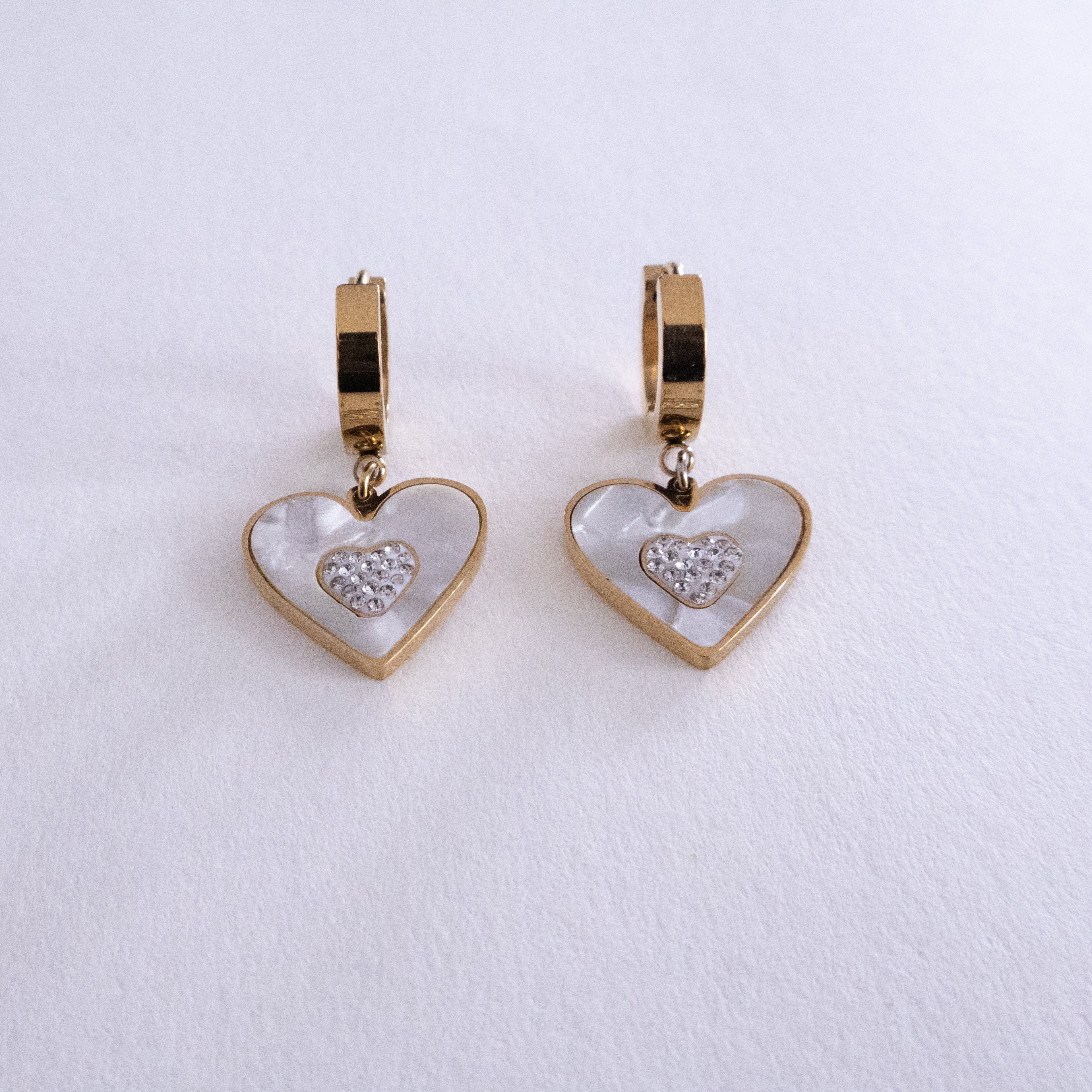 Heart-shaped earrings with gold and white design on a light gray background