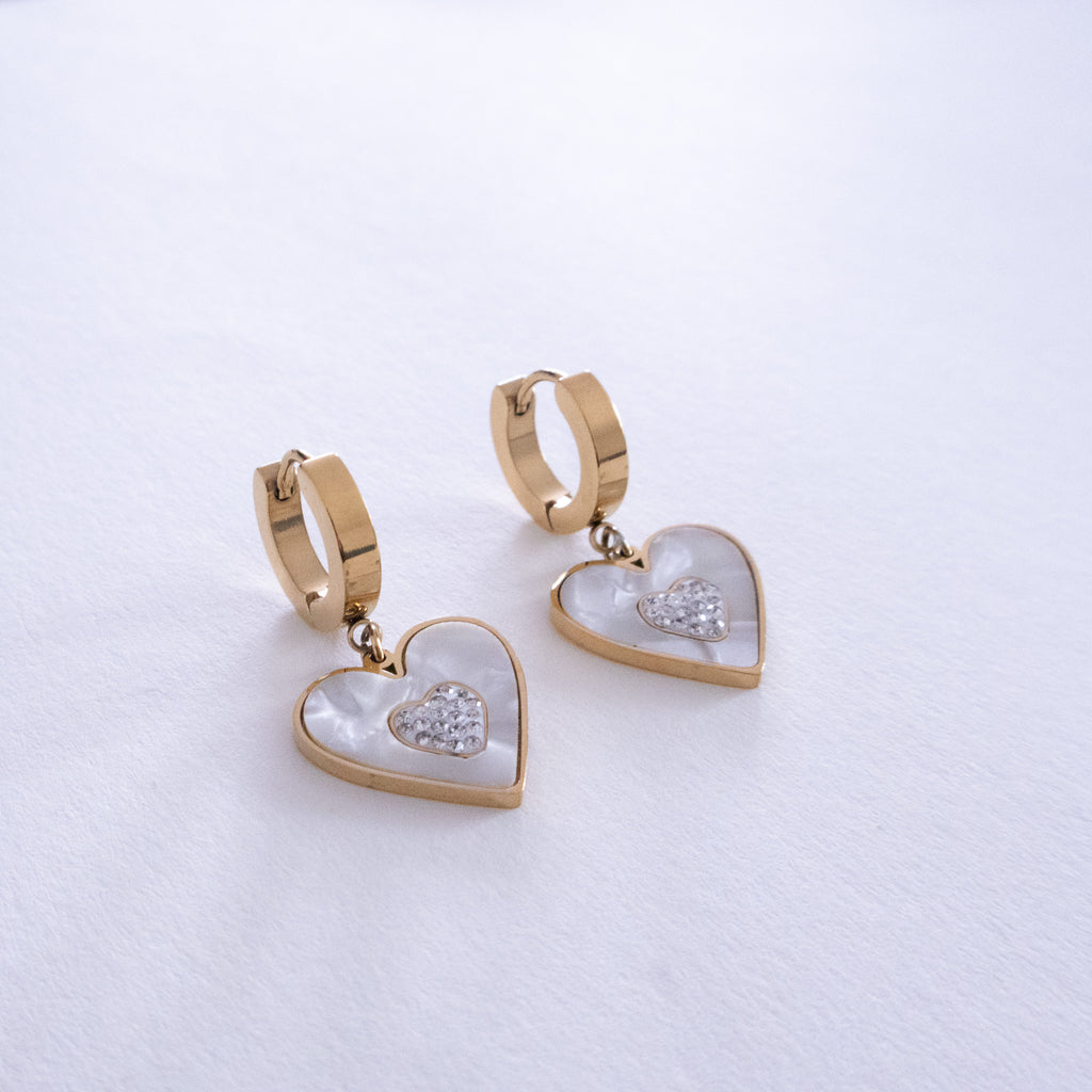 Heart-shaped earrings with gold and white details on a light gray background