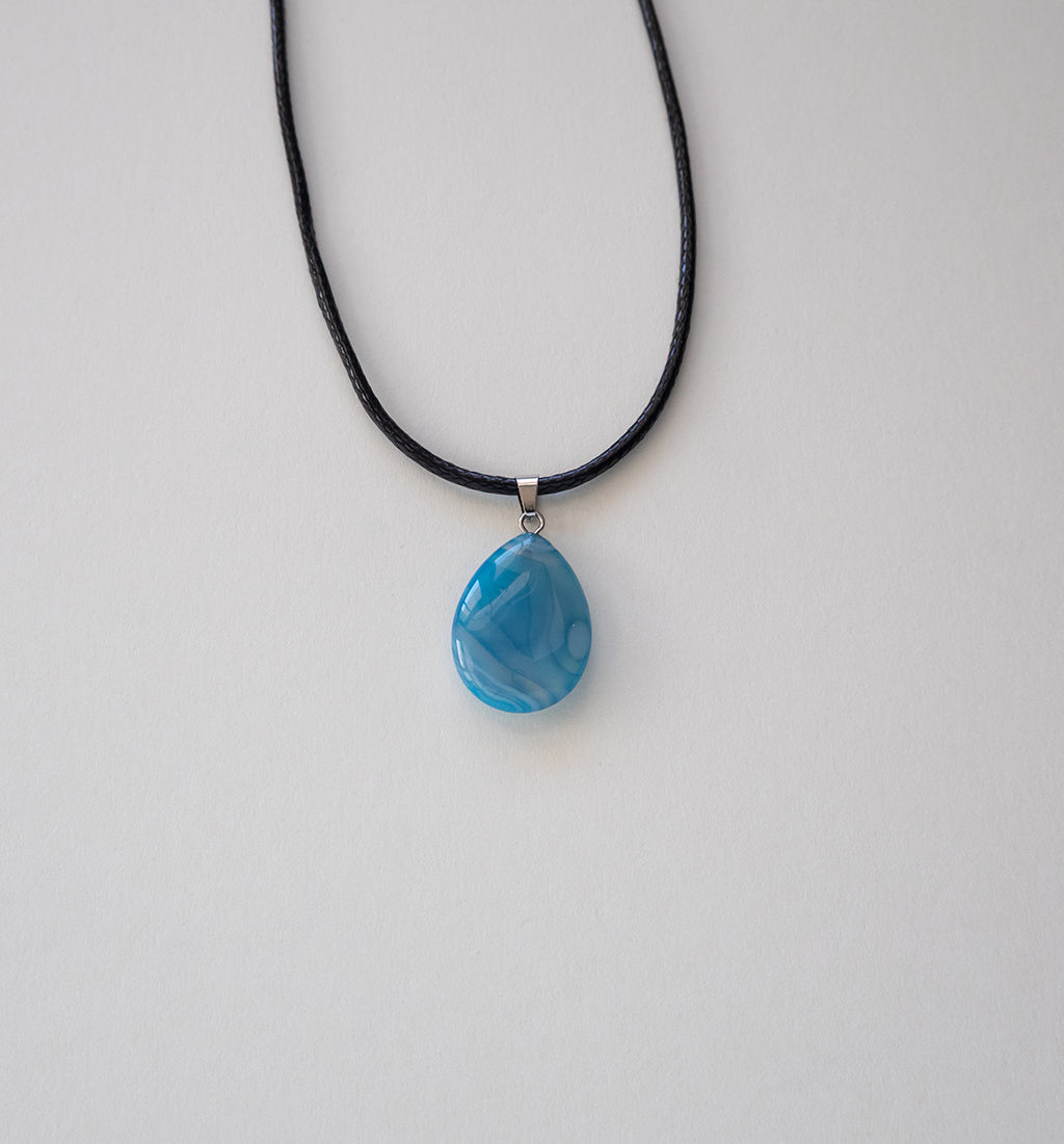 Colar com pendente em forma de lágrima de pedra azul natural e cordão preto.