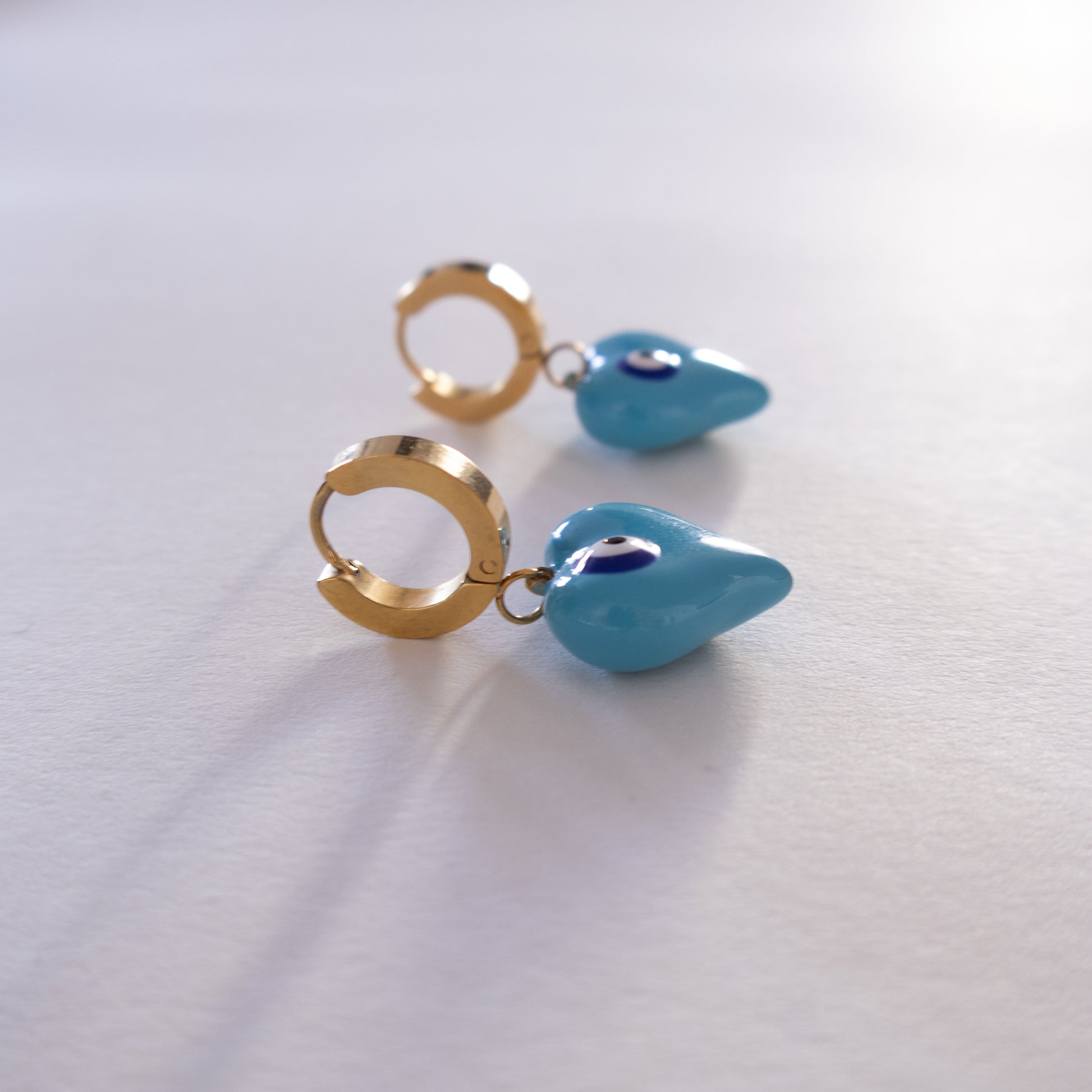 Pair of gold hoop earrings with blue teardrop charms on a white background
