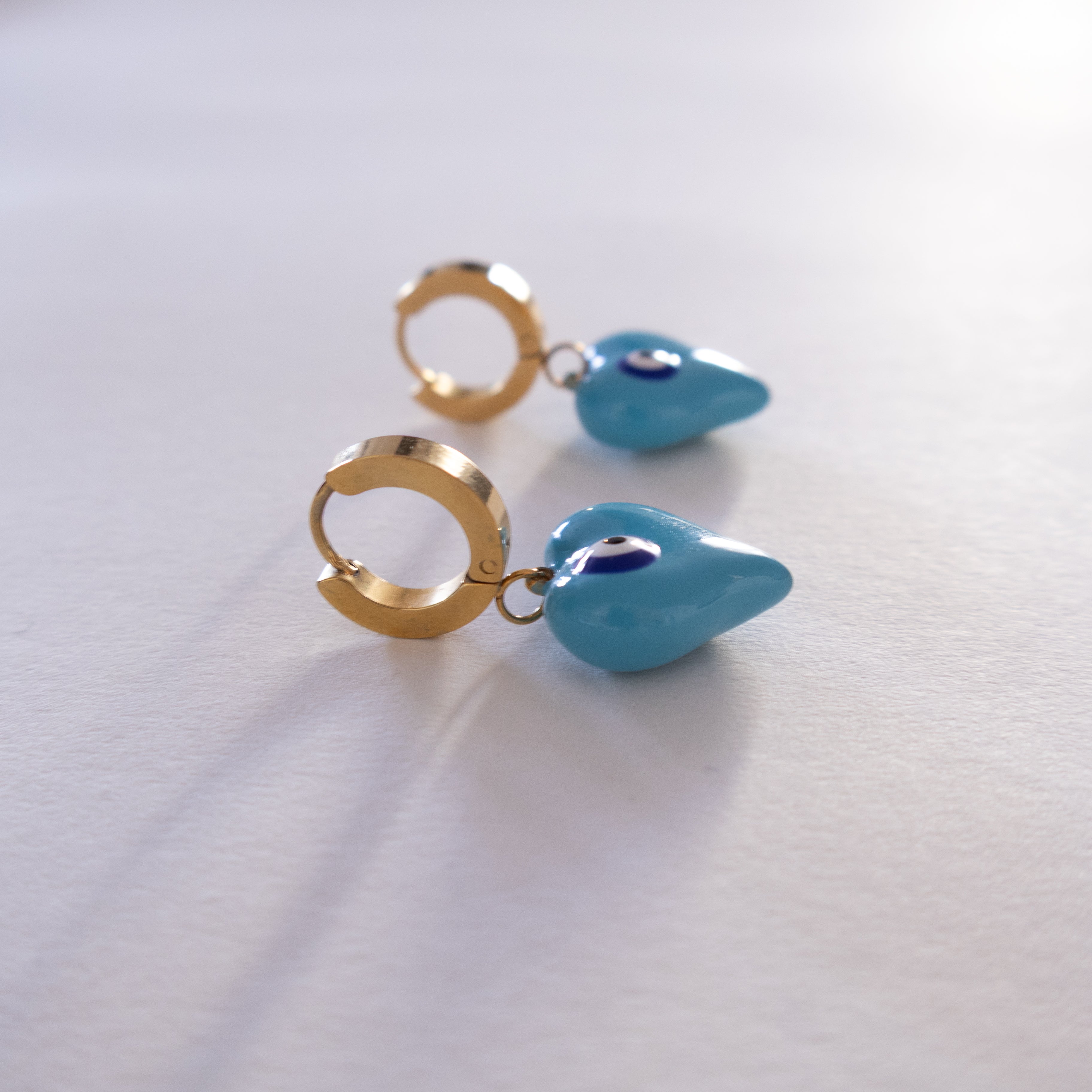 Pair of gold hoop earrings with blue teardrop charms on a white background
