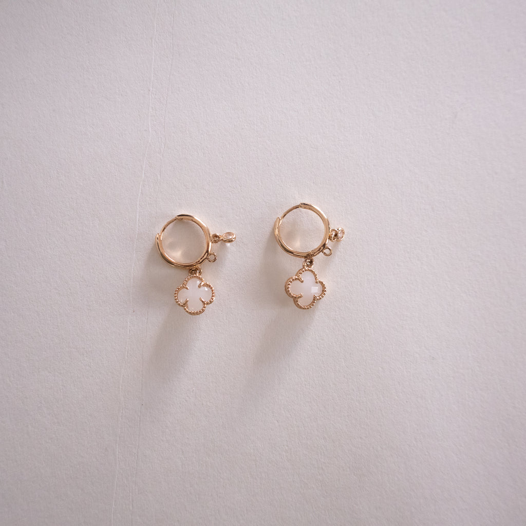 Pair of gold earrings with clover-shaped charms on a light gray background
