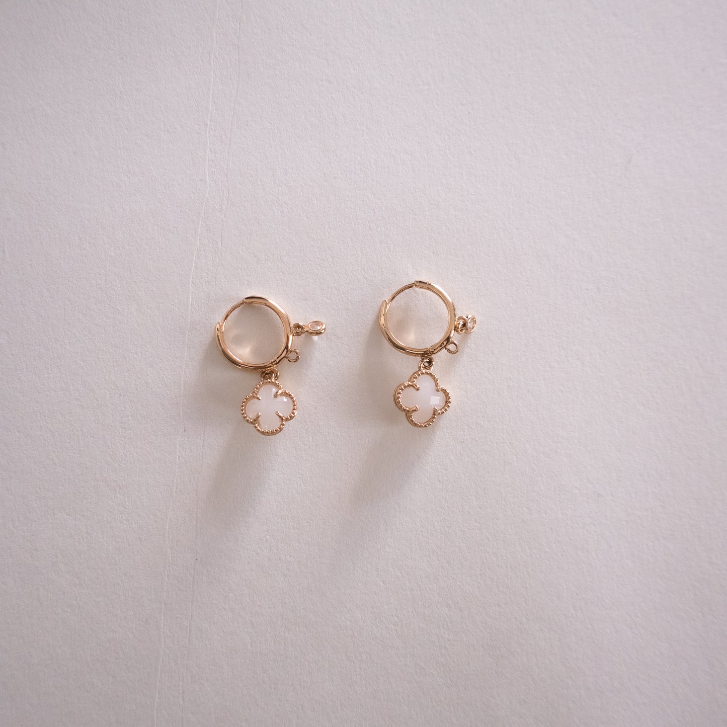 Pair of gold earrings with clover-shaped charms on a light gray background