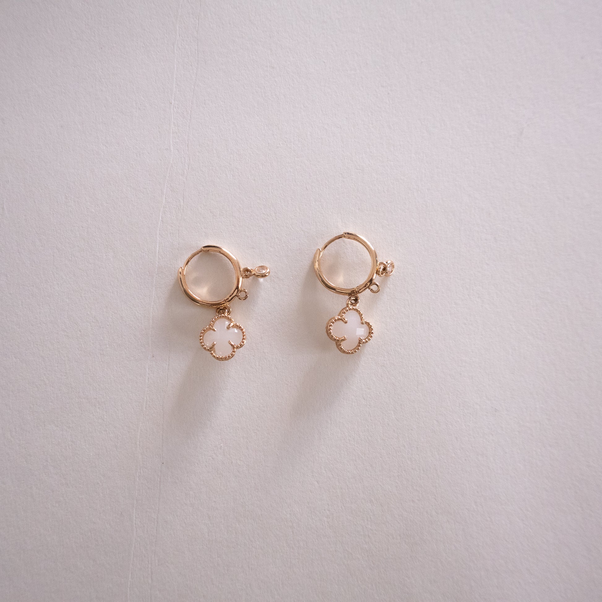 Pair of gold earrings with clover-shaped charms on a light gray background