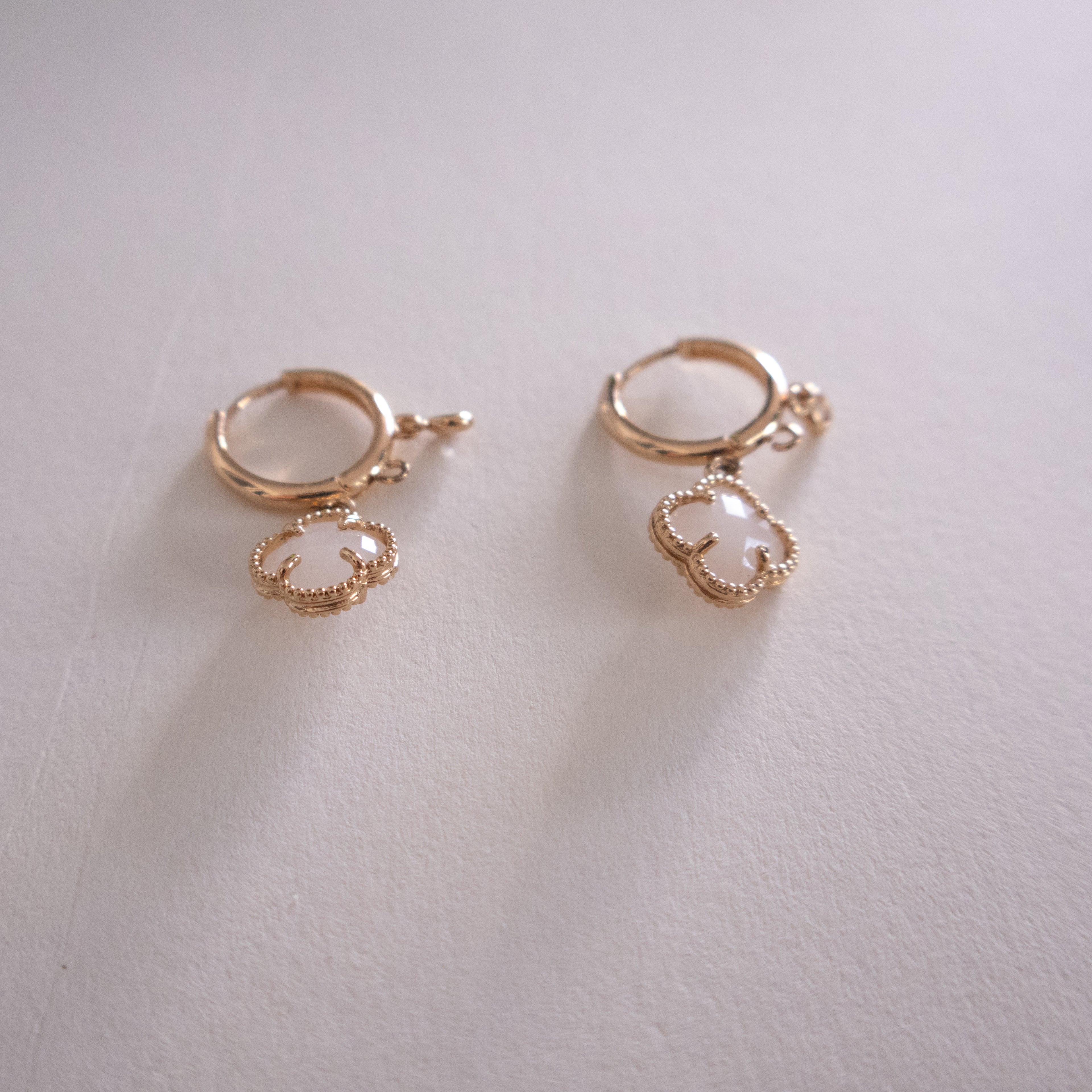 Pair of gold hoop earrings with a pearl-like center on a light gray background