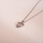 Heart-shaped silver pendant necklace on a light pink background