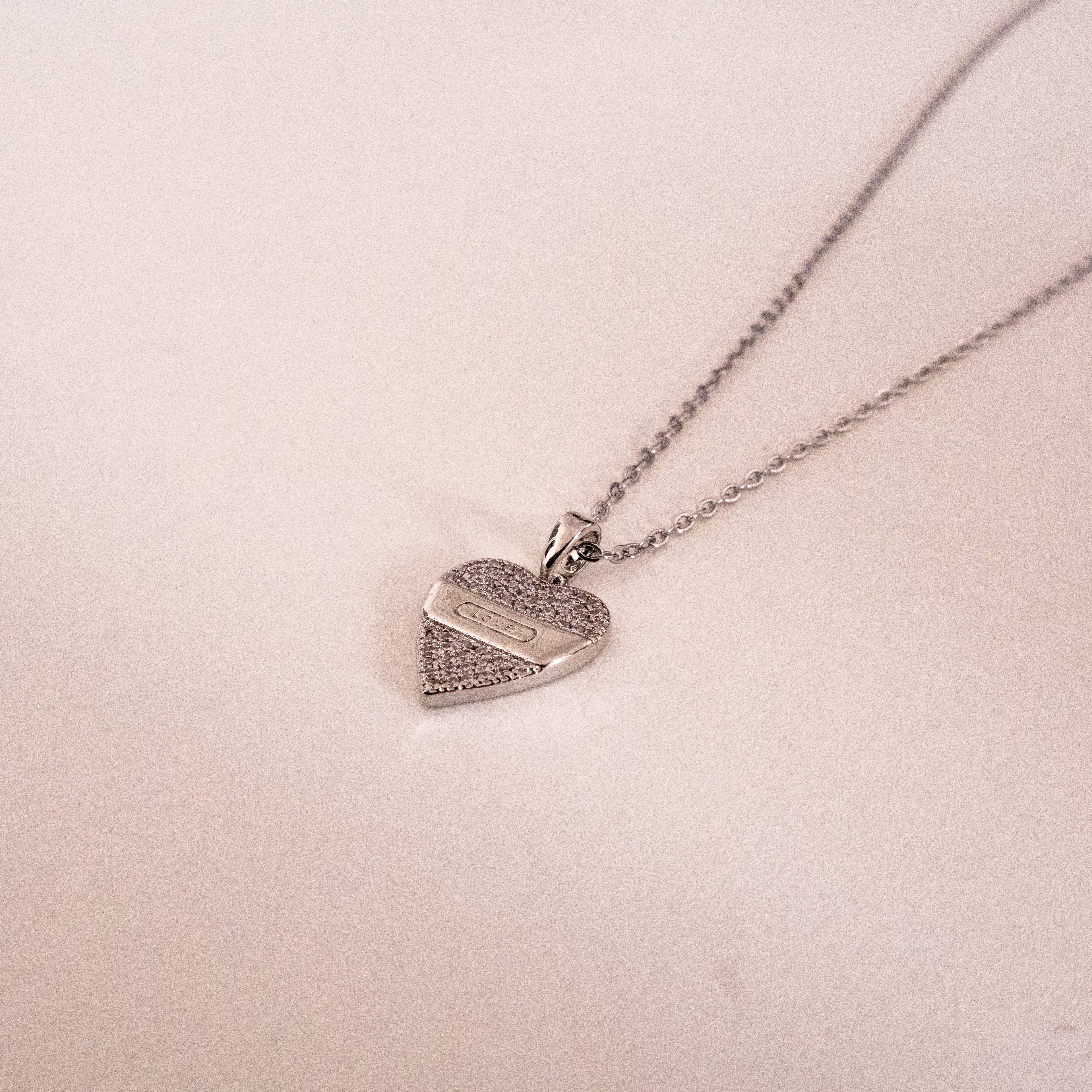 Heart-shaped silver pendant necklace on a light pink background