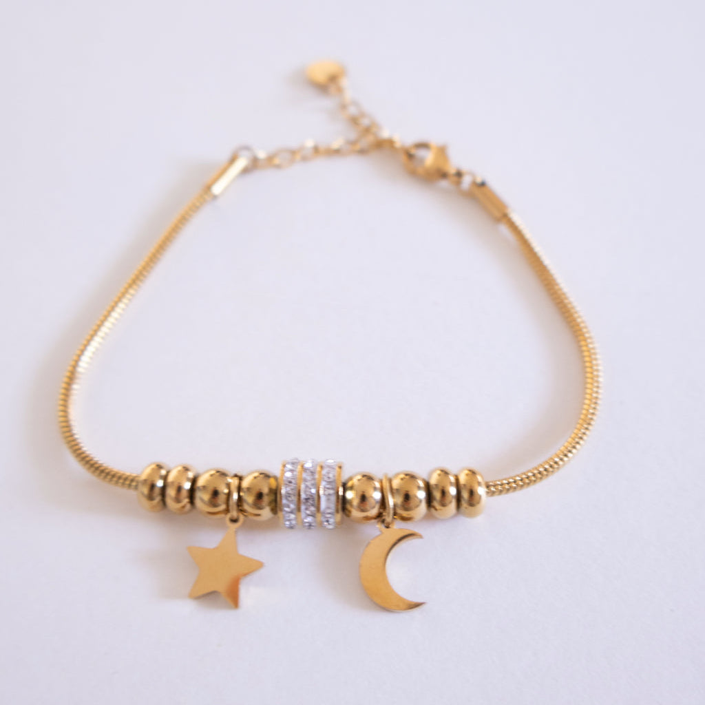 Gold bracelet with star and moon charms on a light gray background