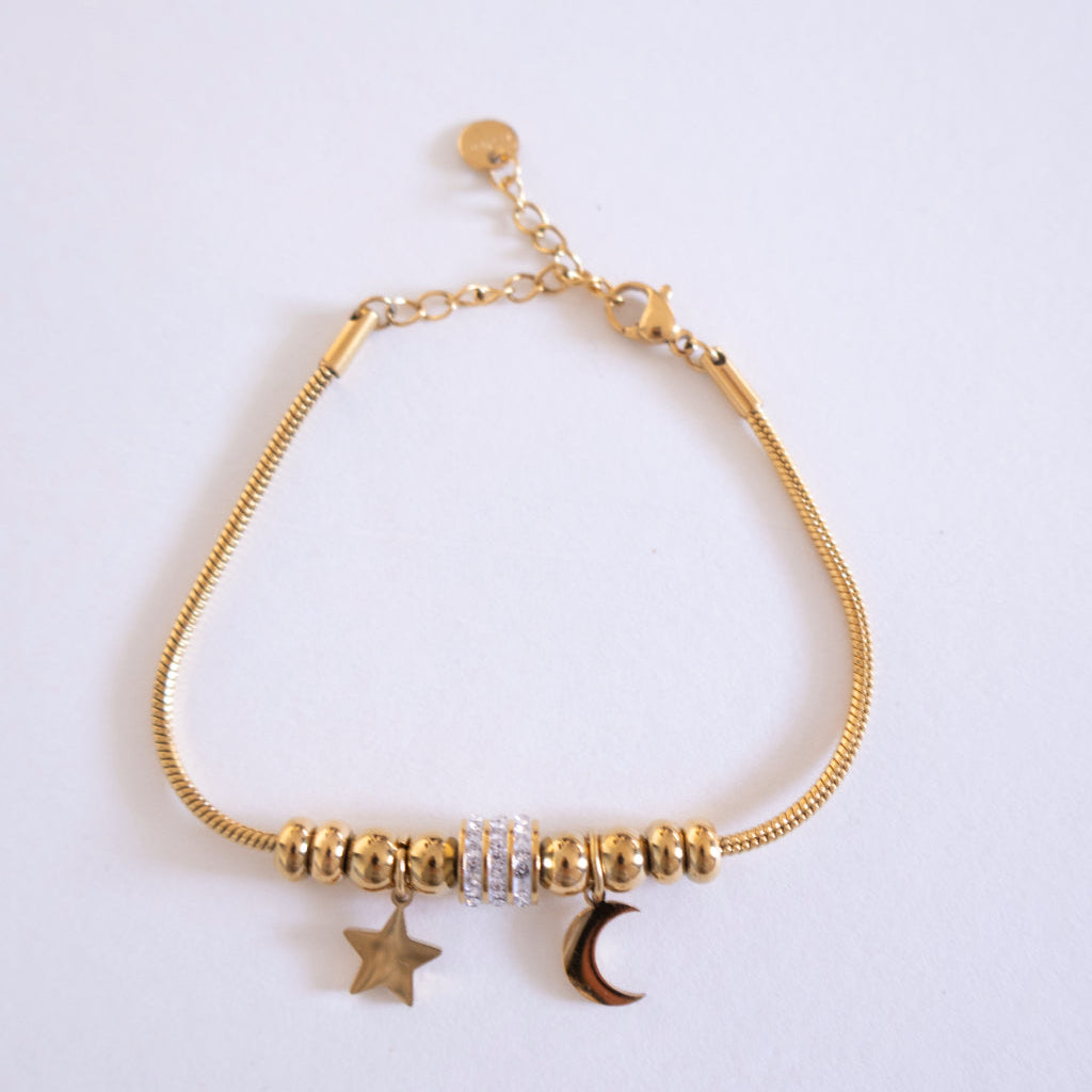 Gold bracelet with star and moon charms on a light gray background