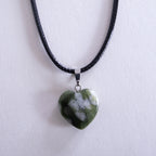 Heart-shaped green stone pendant on a black cord against a white background