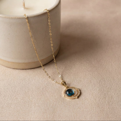 Necklace with a blue gemstone pendant in front of a lit candle in a white container on a beige fabric background