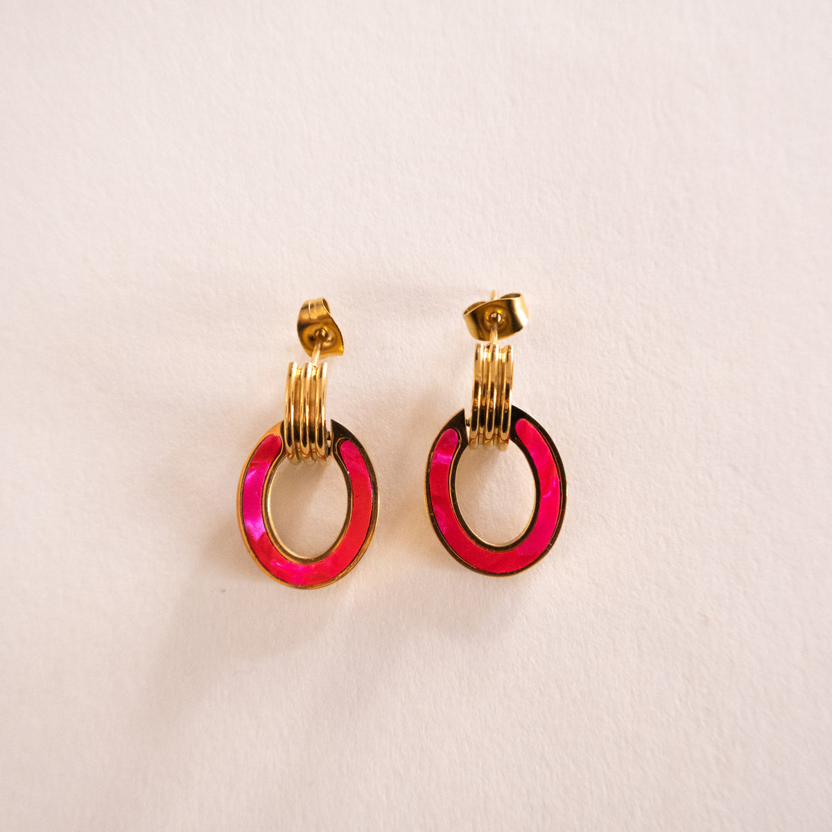 Pair of earrings with gold loops and pink circular accents on a beige background