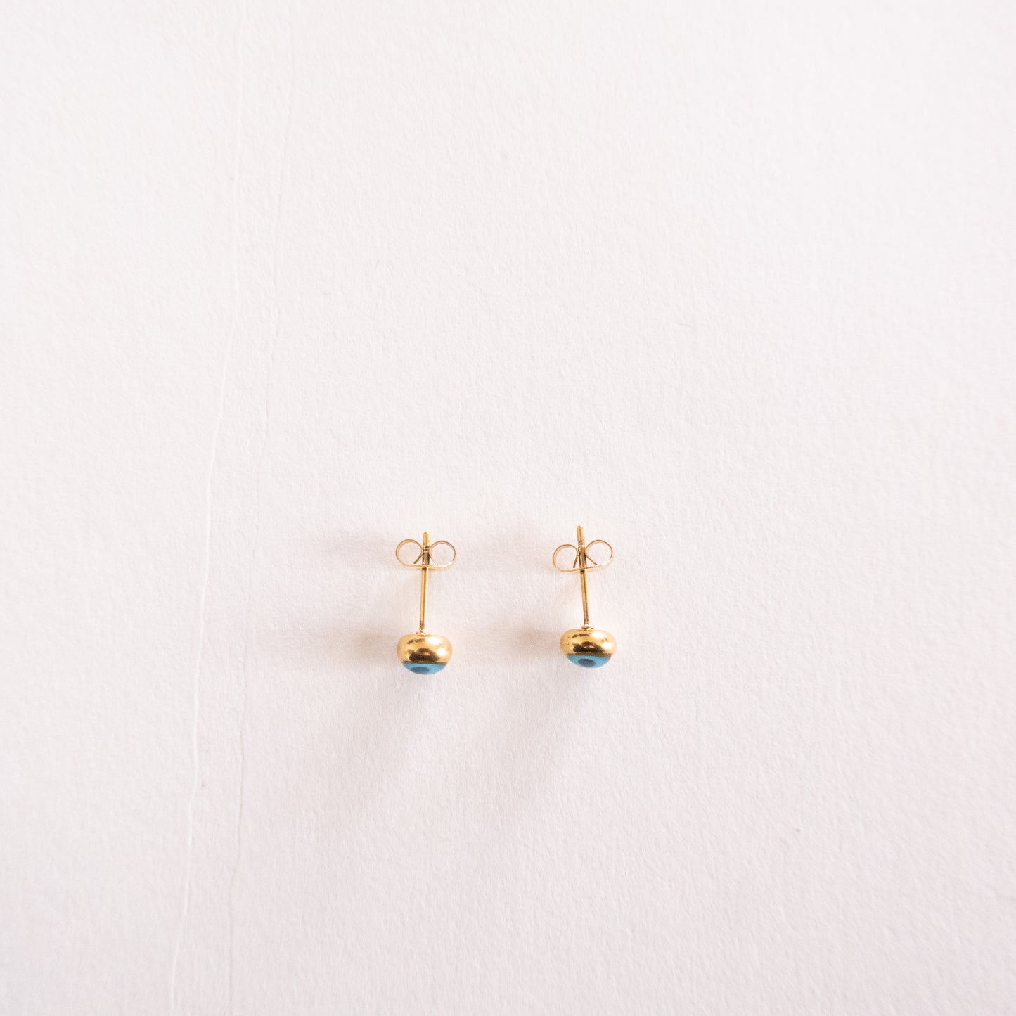 Pair of gold earrings with blue gemstones on a light pink background
