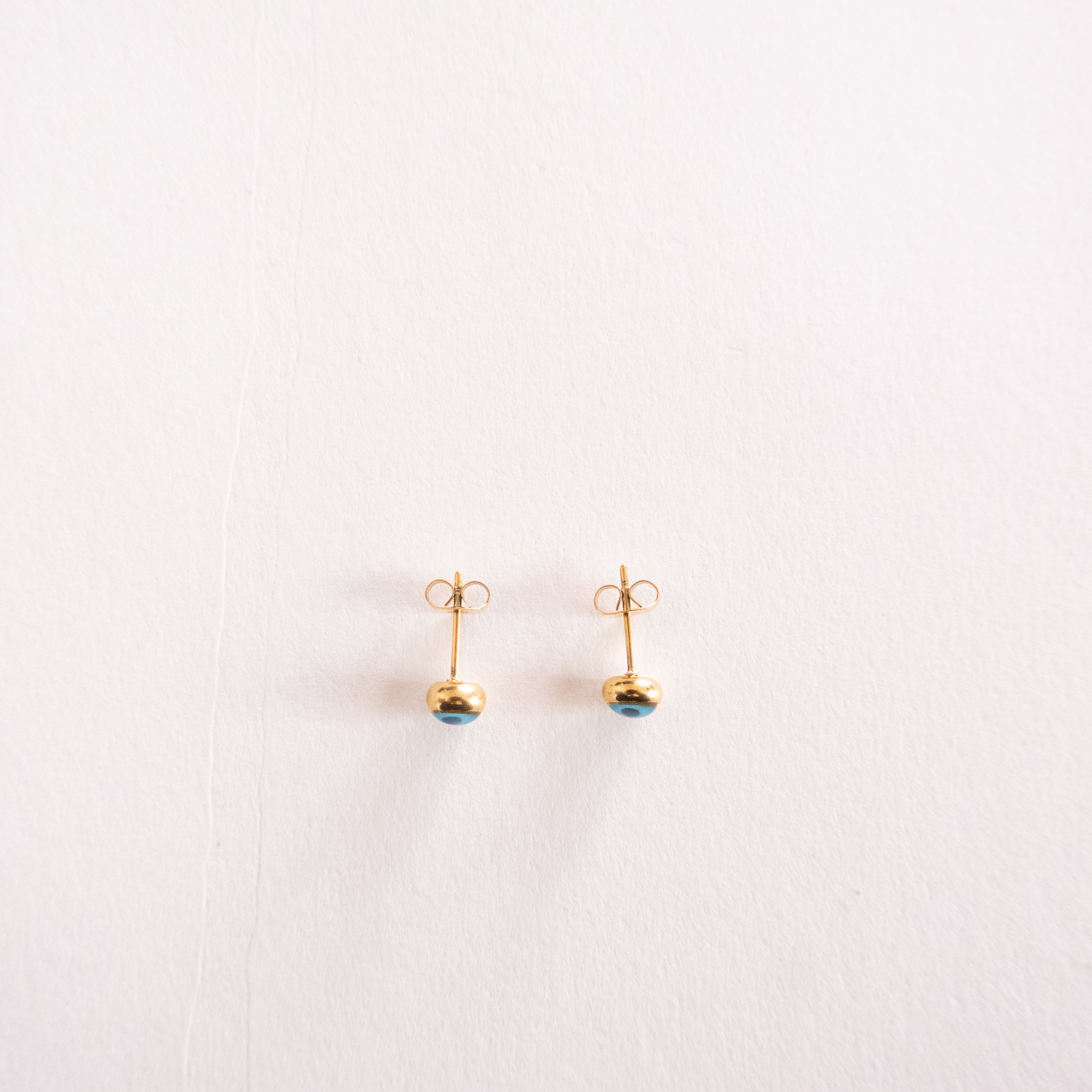 Pair of gold earrings with blue gemstones on a light pink background