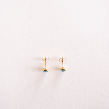 Pair of gold earrings with blue gemstones on a light pink background