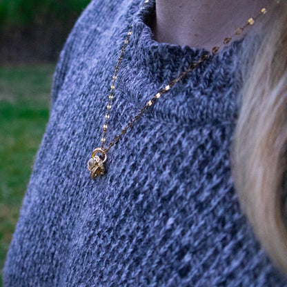 Person wearing a blue knitted sweater with a gold necklace outdoors