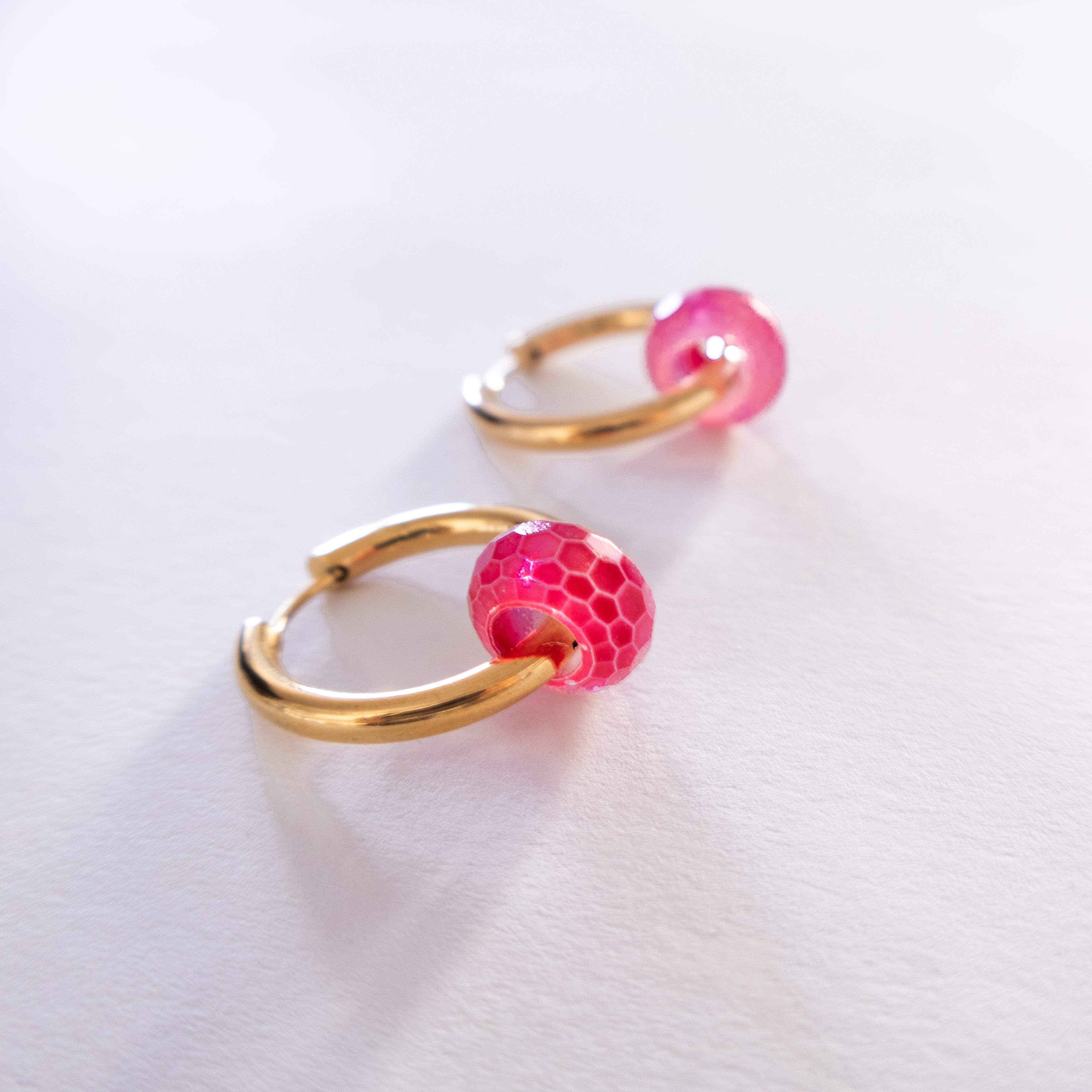 Gold hoop earrings with pink spherical charms on a white background