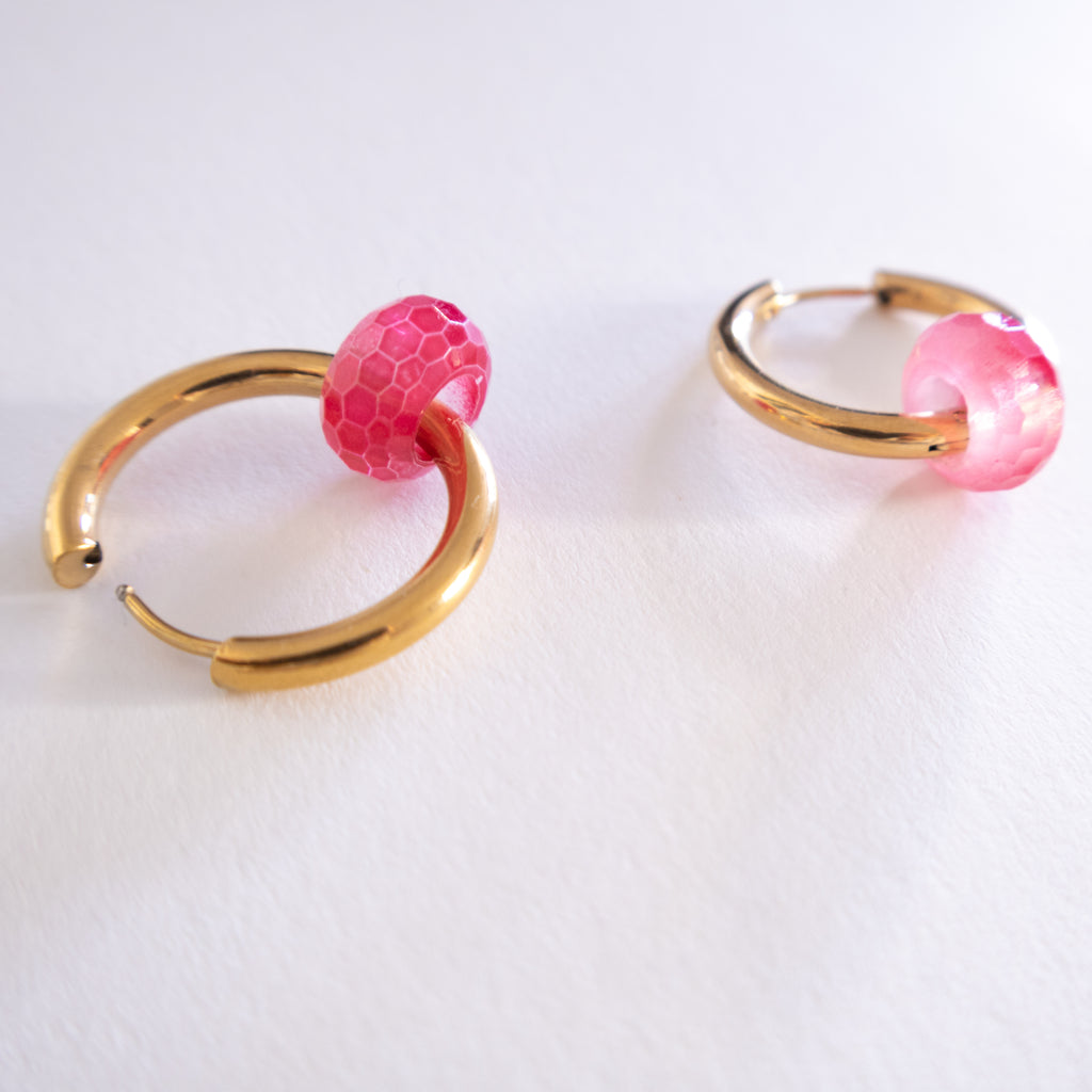 Gold hoop earrings with pink spherical charms on a white background