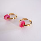 Gold hoop earrings with pink beads on a white background