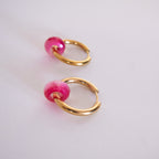 Gold hoop earrings with pink beads on a light gray background