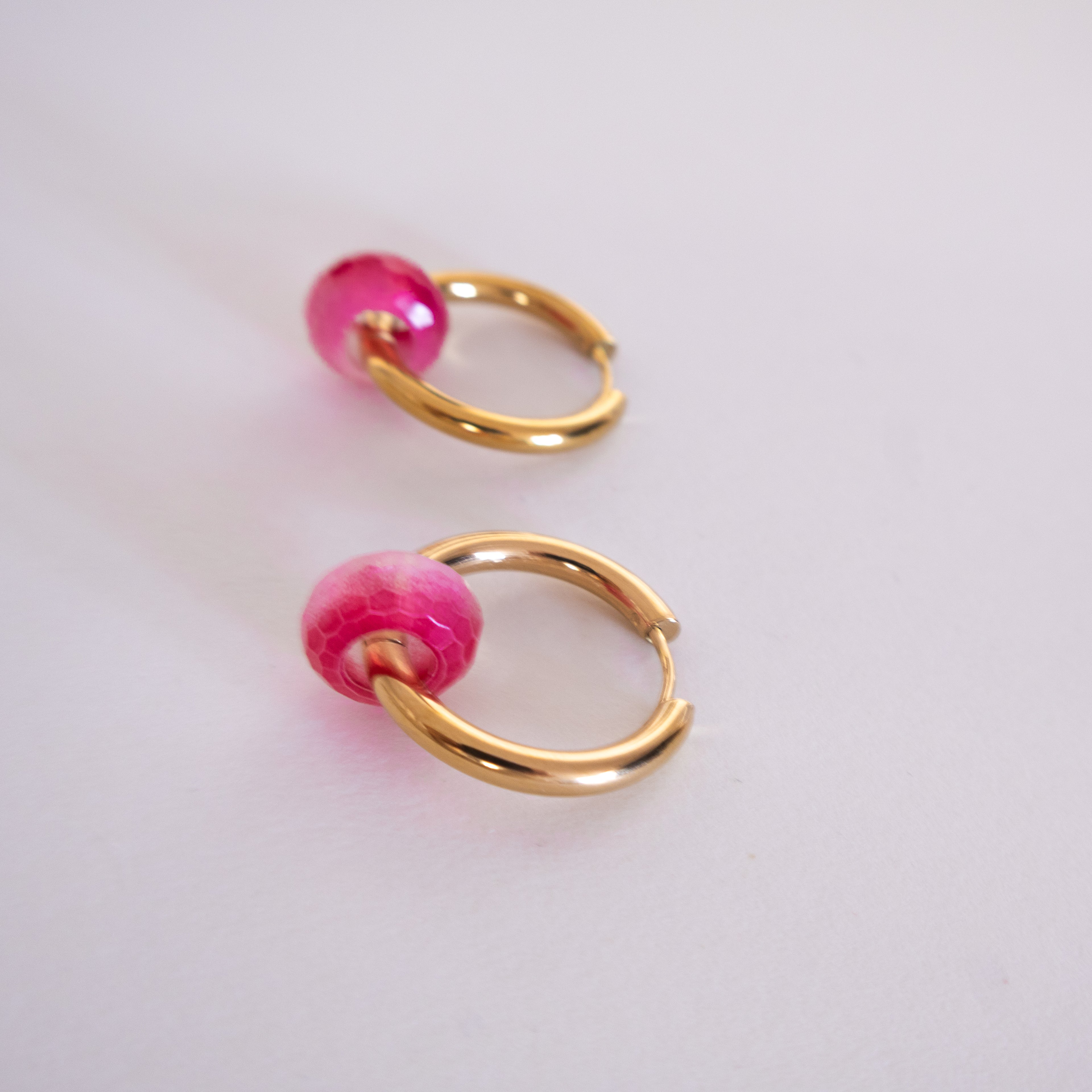 Gold hoop earrings with pink beads on a light gray background