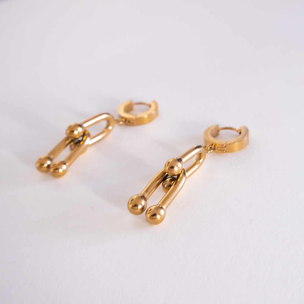 Gold hoop earrings with chain and ball details on a white background