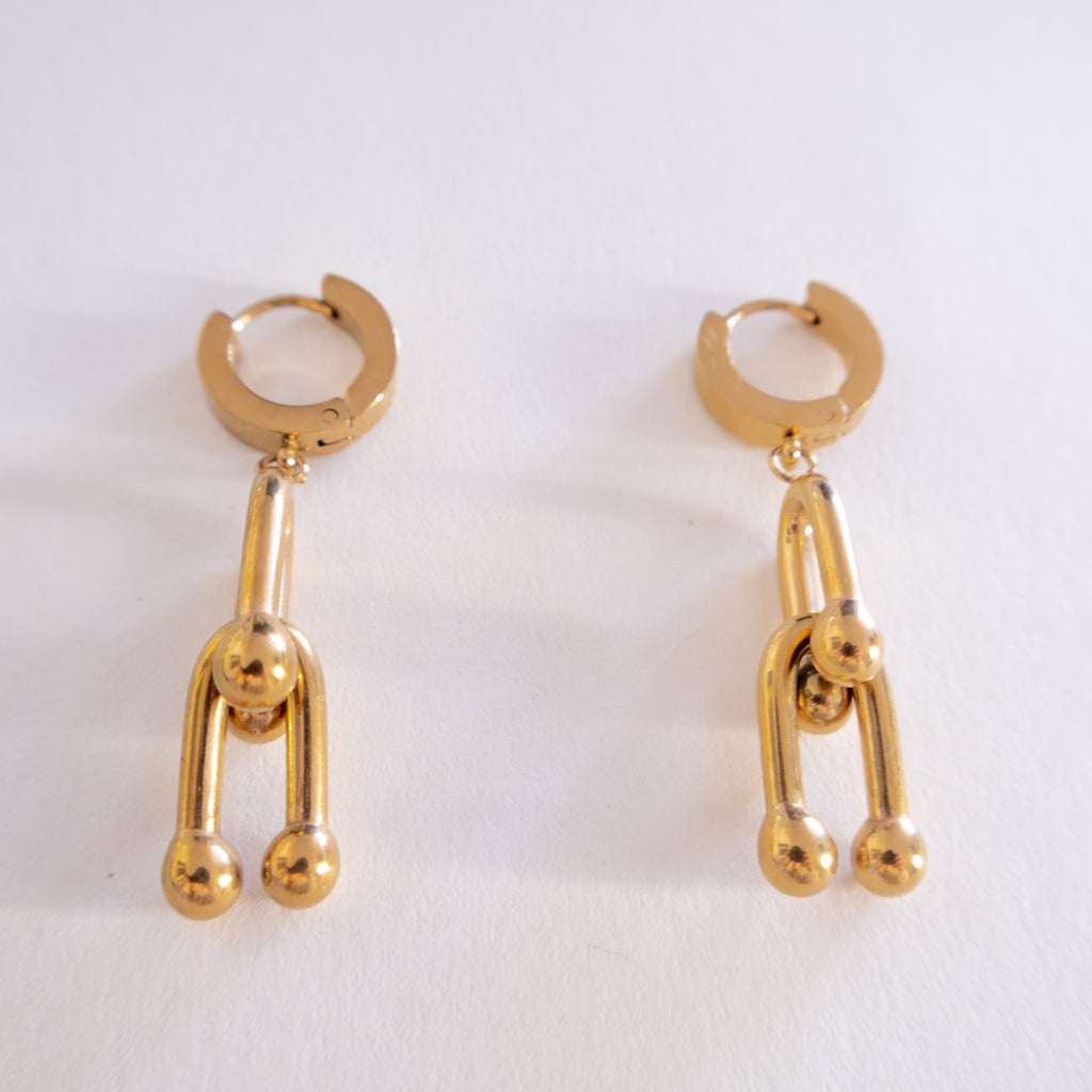 Pair of gold hoop earrings with dangling ball charms on a white background