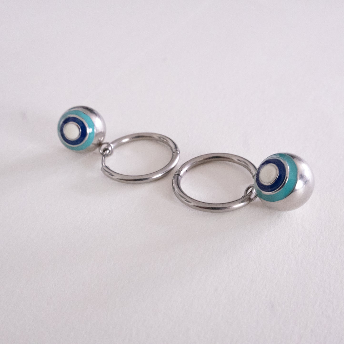 Pair of silver hoop earrings with blue and white circular accents on a light gray background