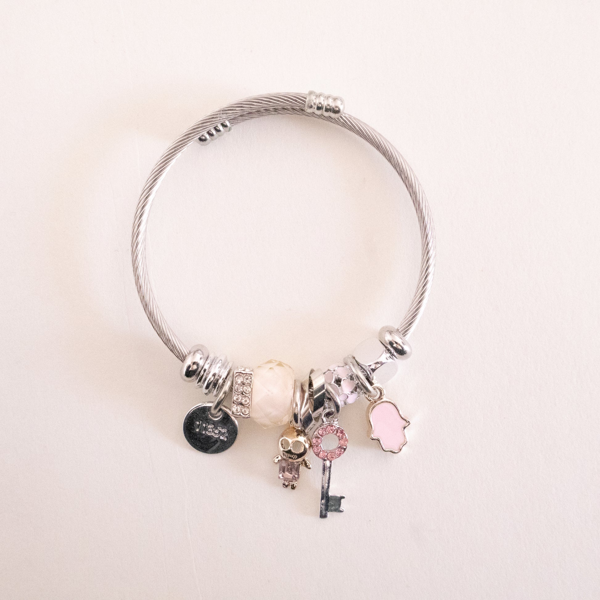 Silver bracelet with various charms on a light pink background