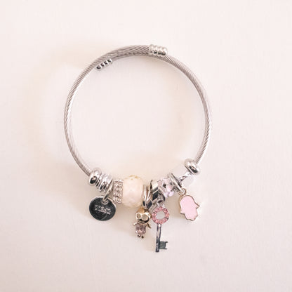 Silver bracelet with various charms on a light pink background