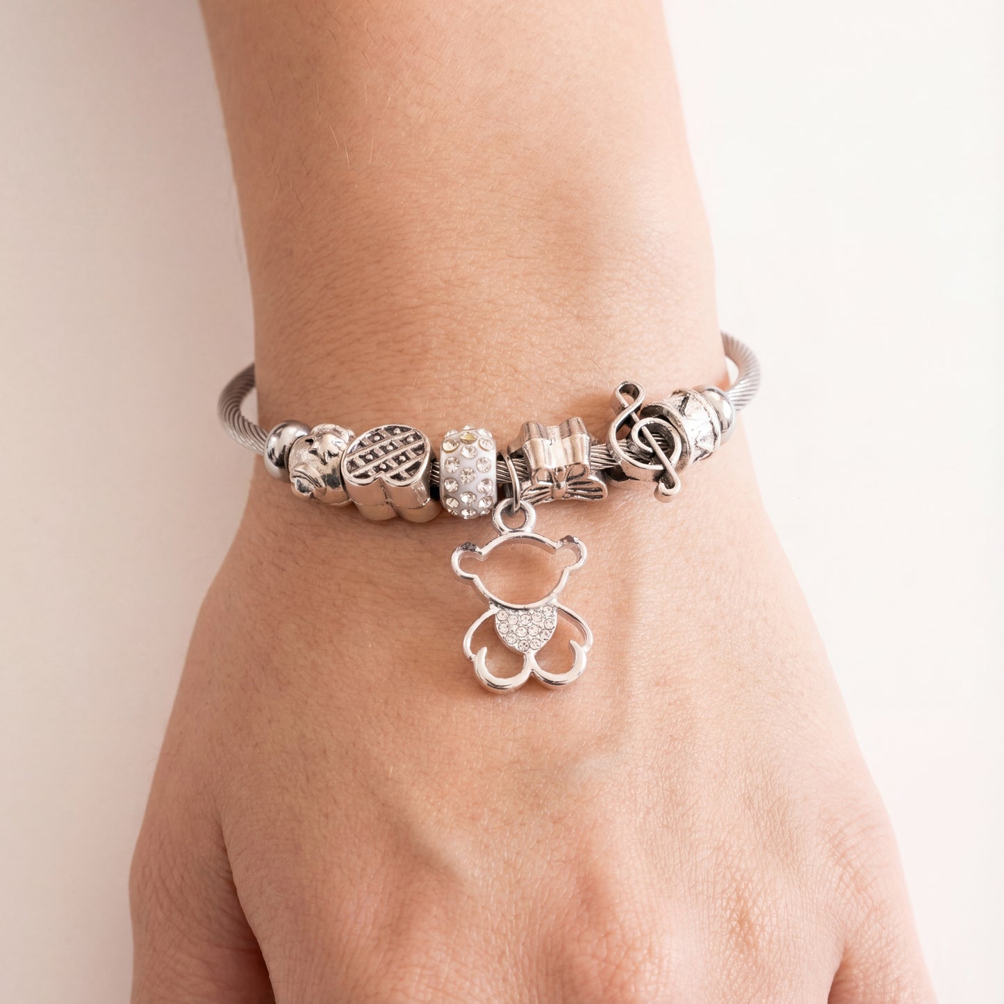Silver bracelet with various charms on a wrist against a light background