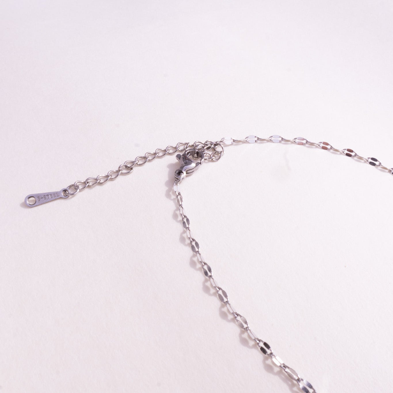 Silver chain necklace on a light pink background