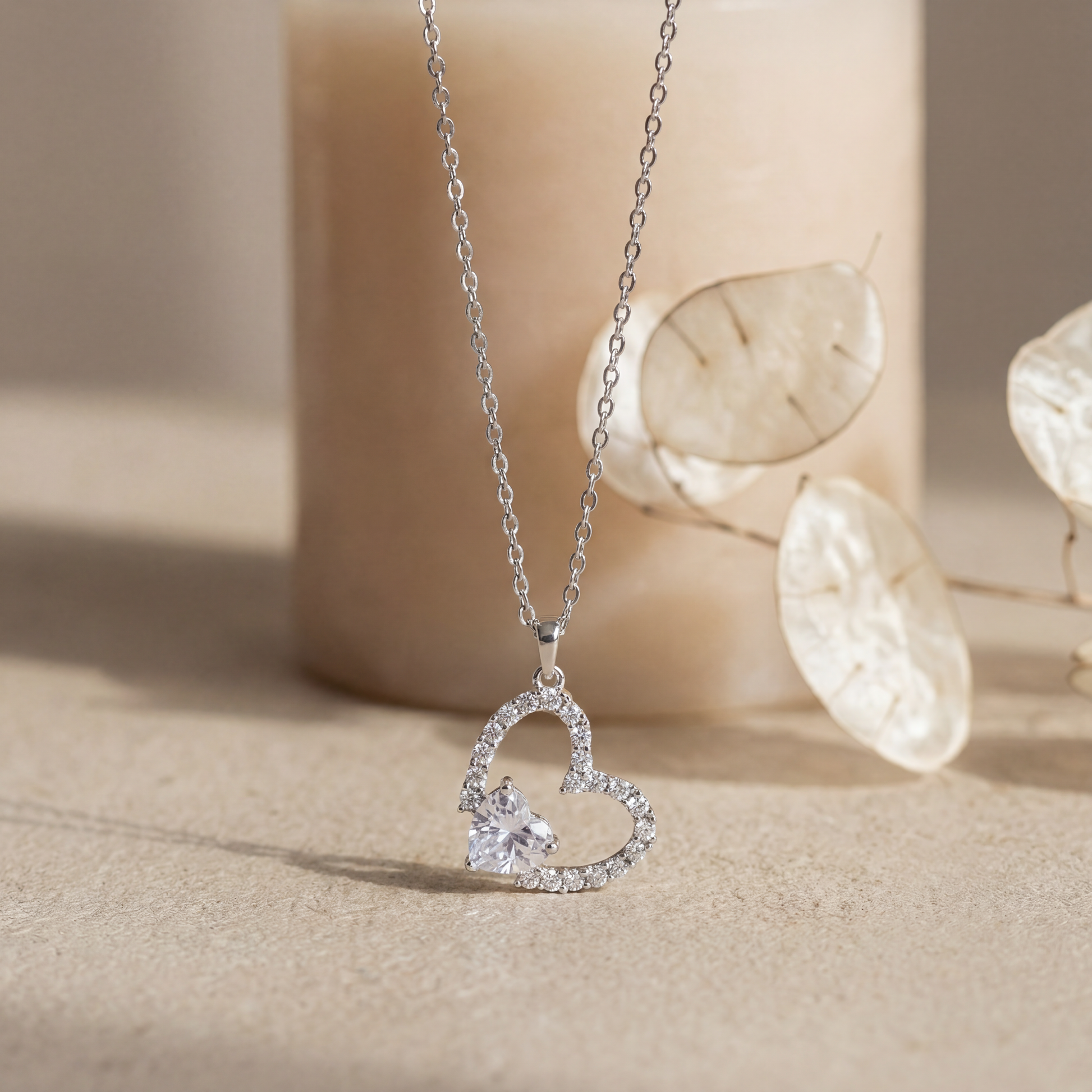 Silver heart-shaped necklace with a small diamond on a beige background