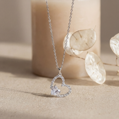 Silver heart-shaped necklace with a small diamond on a beige background