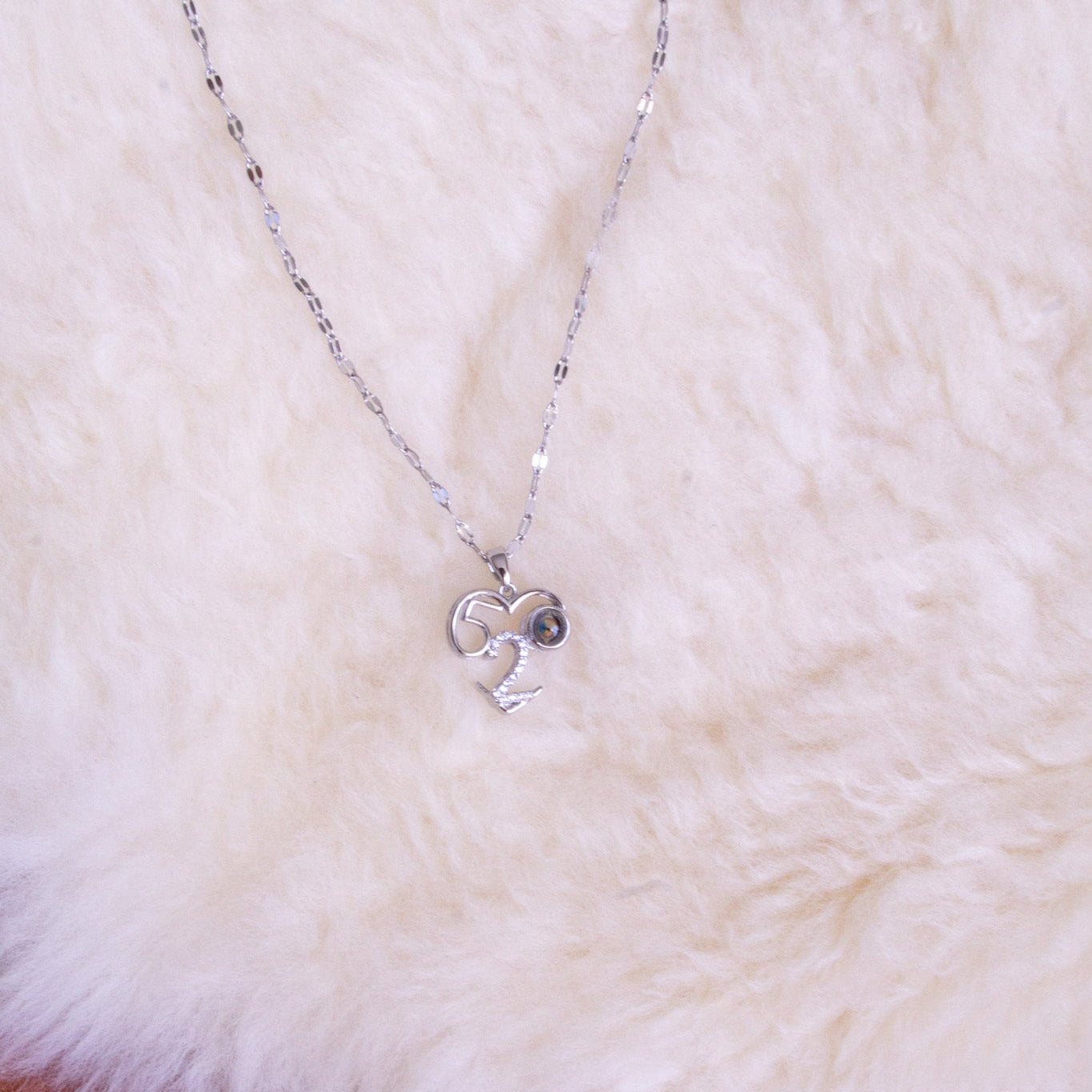 Silver necklace with a heart and number 2 pendant on a fluffy white surface.