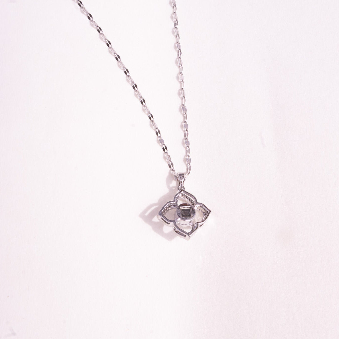 Silver necklace with a star-shaped pendant on a light pink background