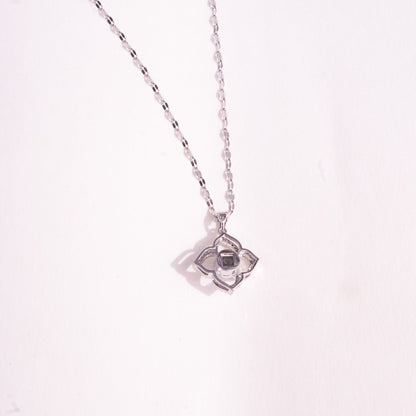 Silver necklace with a star-shaped pendant on a light pink background