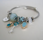 Silver bracelet with various charms on a light gray background