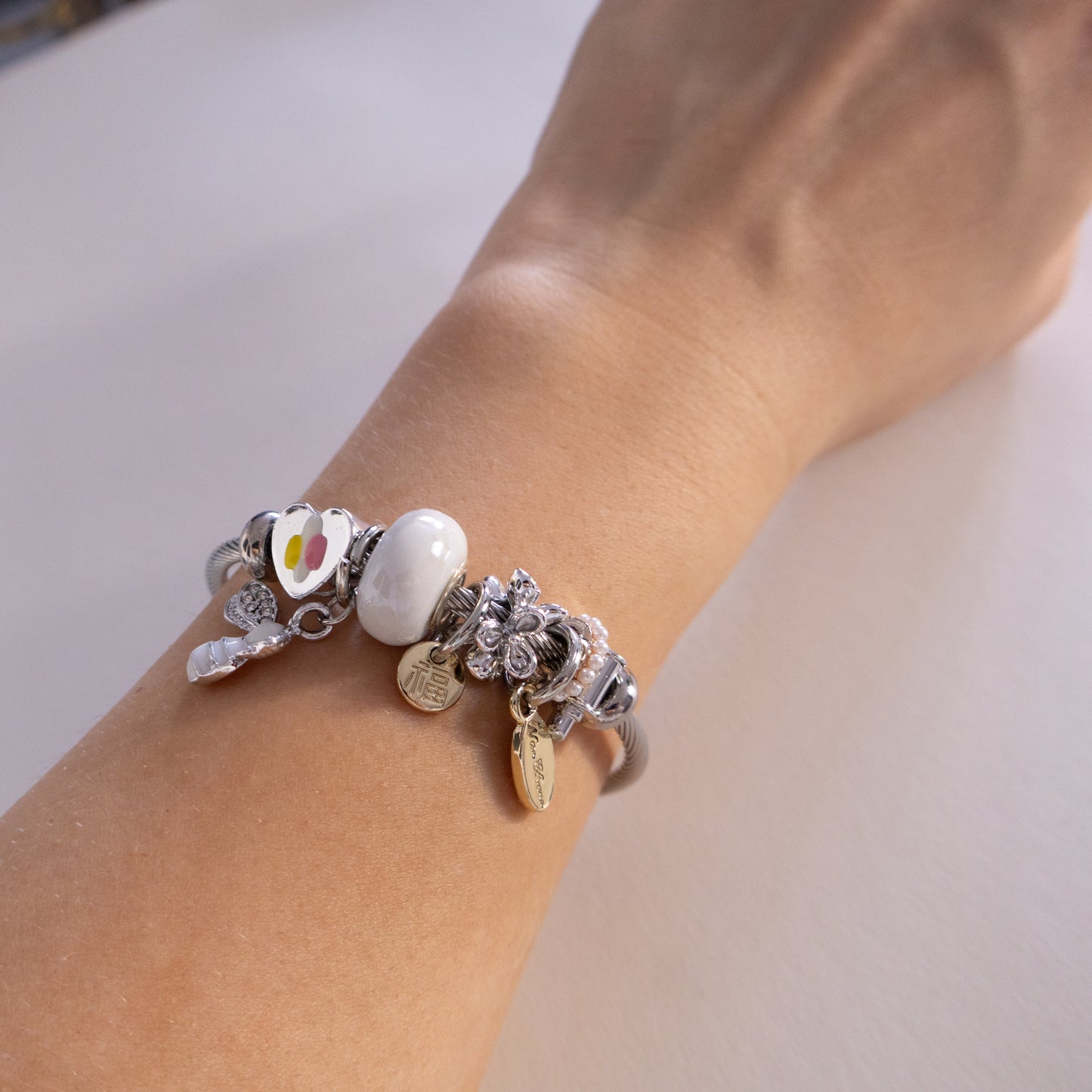 Close-up of a wrist wearing a bracelet with various charms on a neutral background
