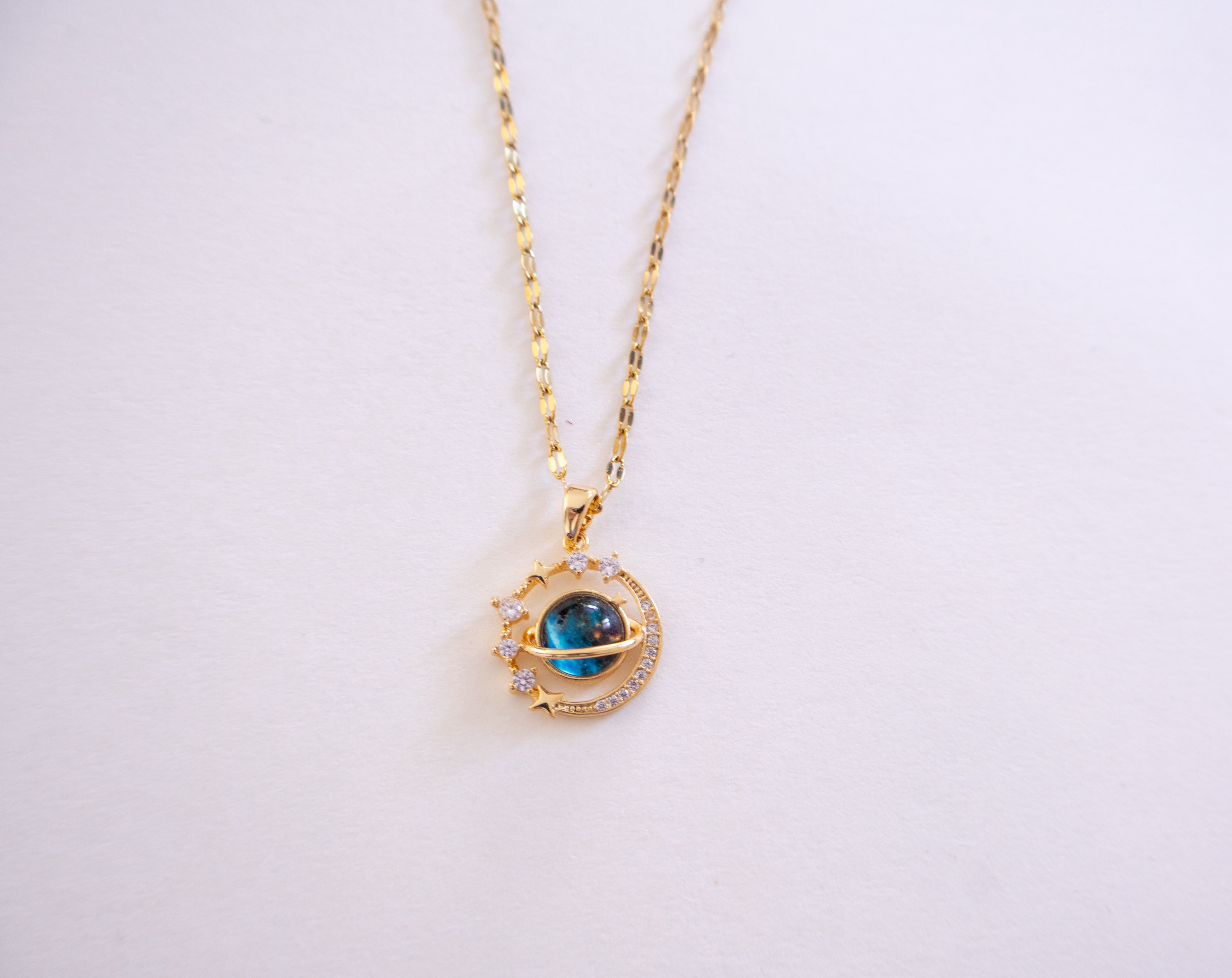 Gold necklace with a blue gemstone pendant on a white background