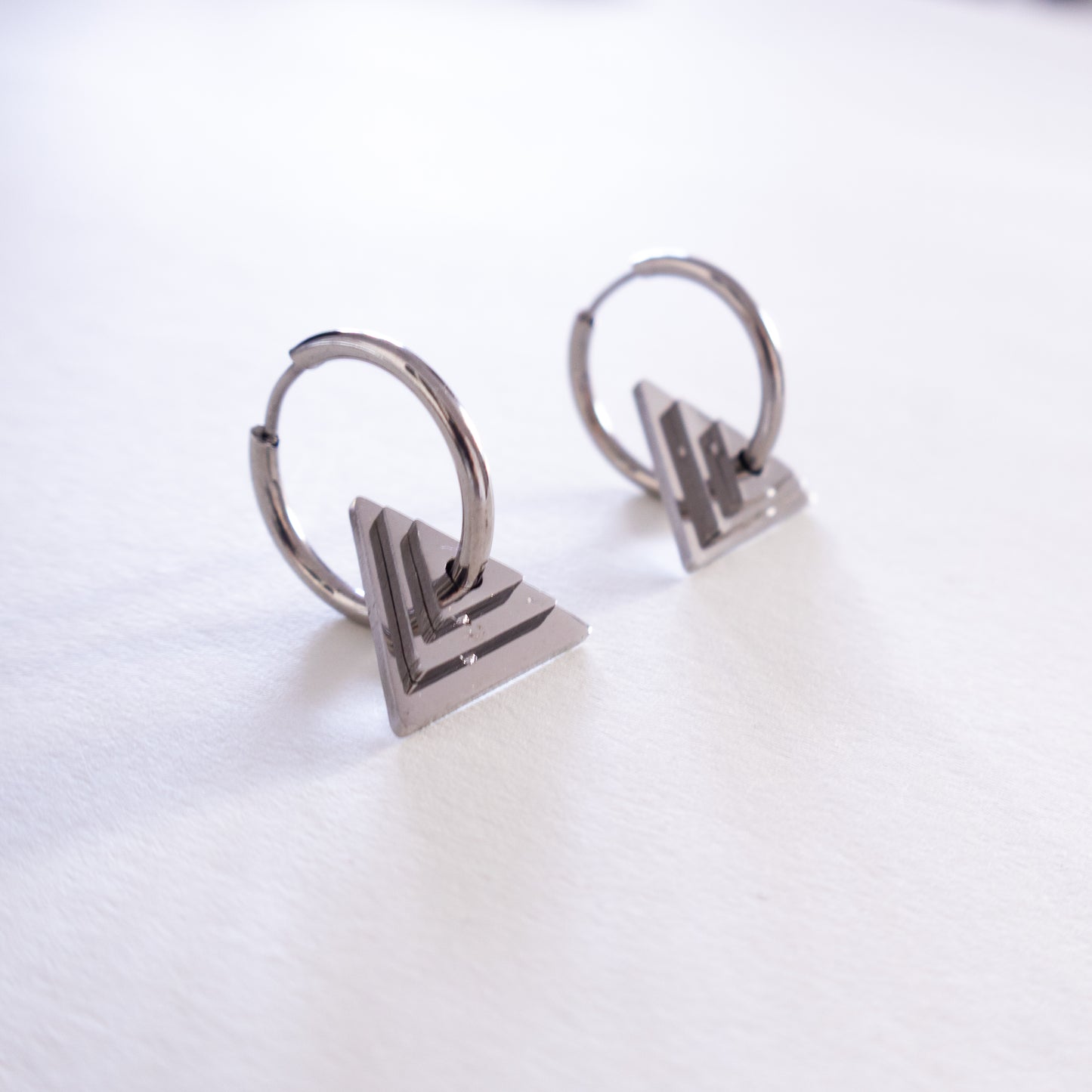 Pair of silver hoop earrings with geometric triangle pendants on a white background
