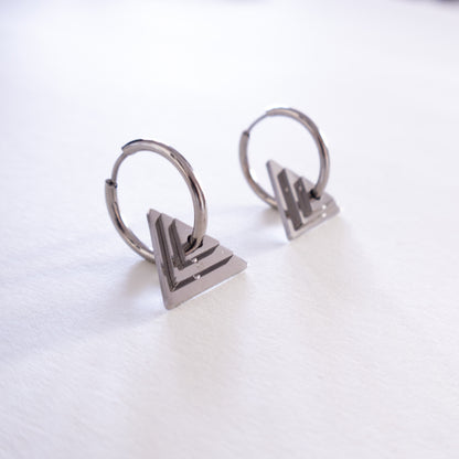 Pair of silver hoop earrings with geometric triangle pendants on a white background