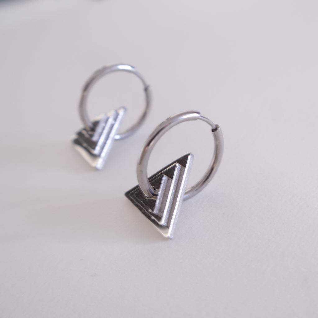 Pair of silver hoop earrings with geometric designs on a light gray background