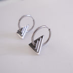 Pair of silver hoop earrings with geometric designs on a light gray background