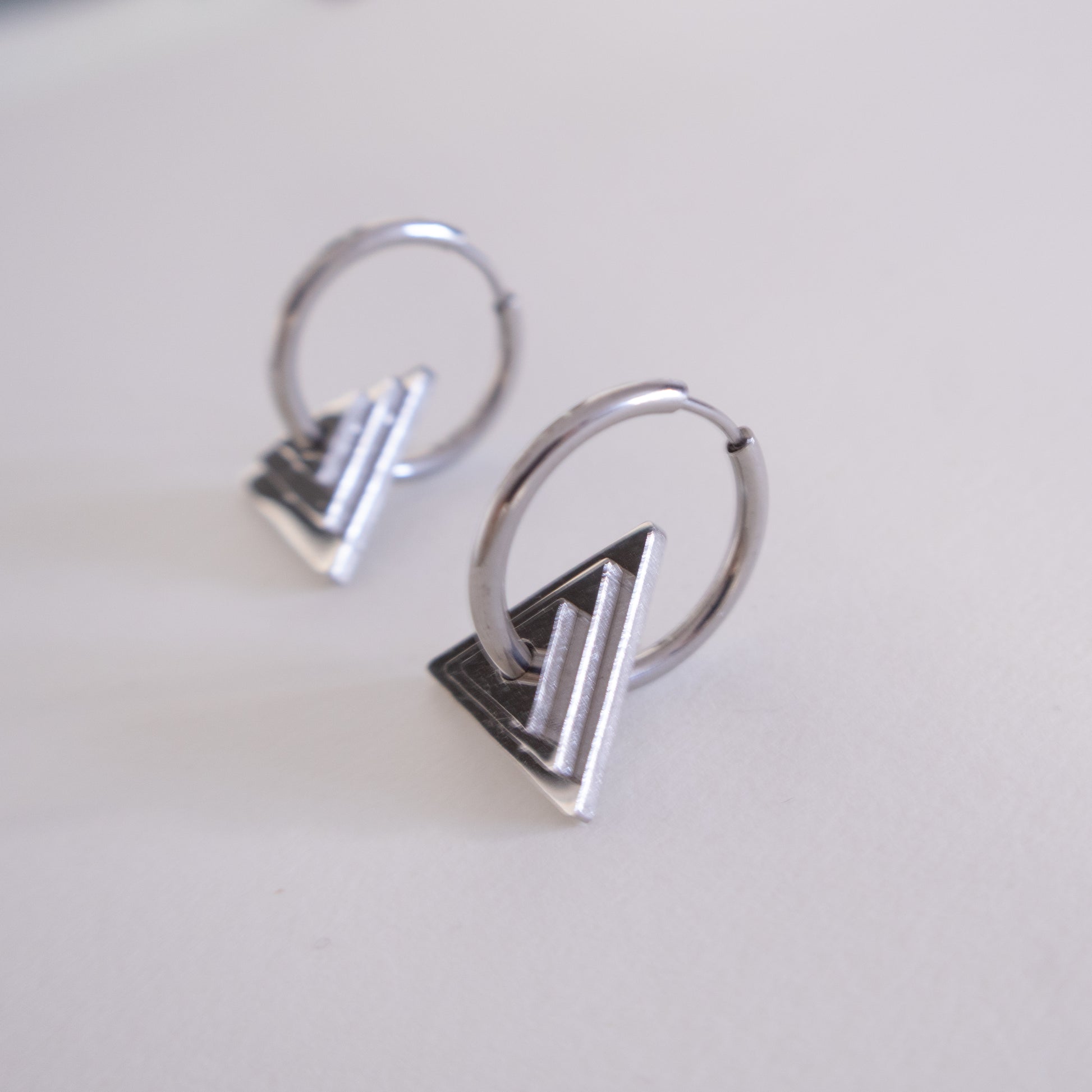 Pair of silver hoop earrings with geometric designs on a light gray background