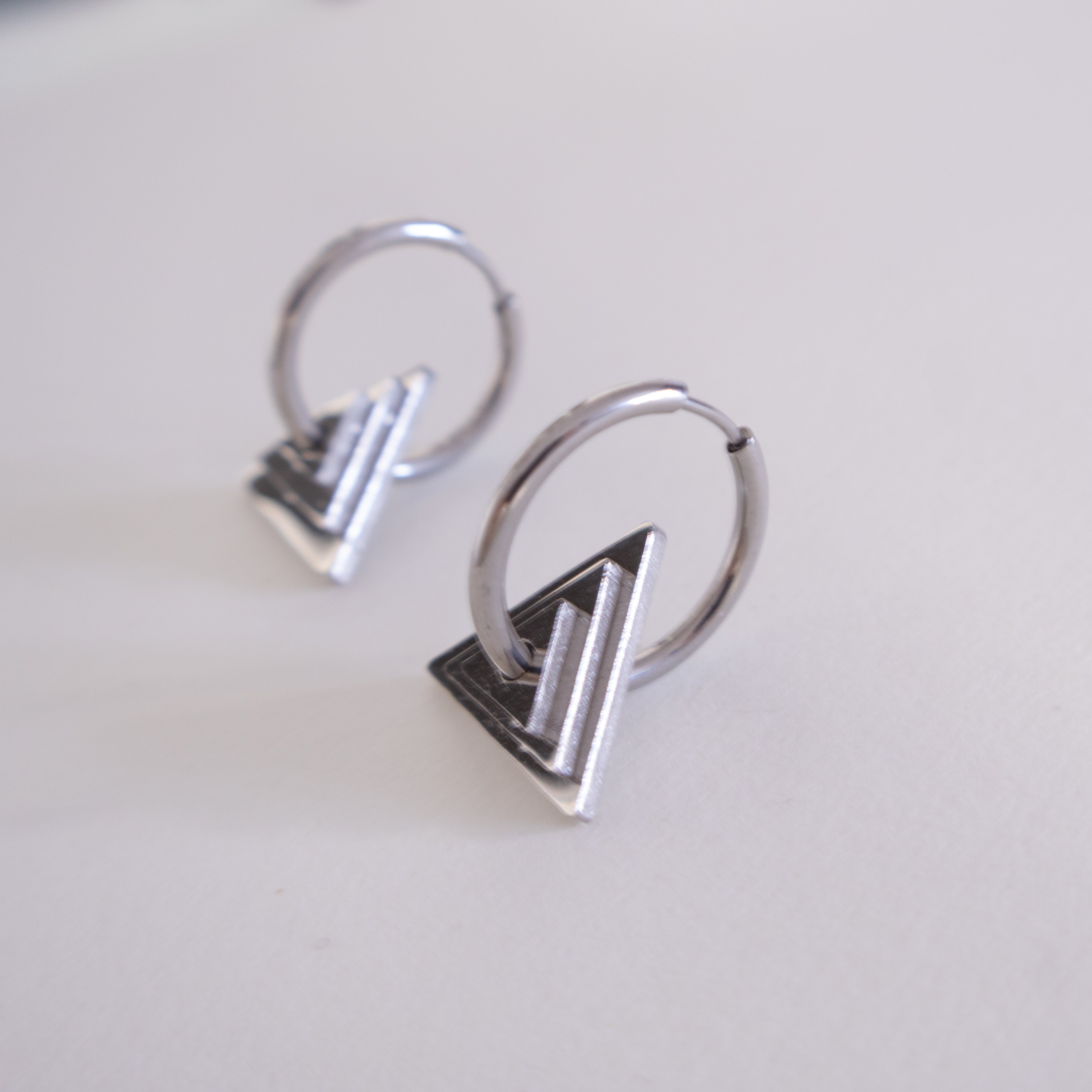 Pair of silver hoop earrings with geometric designs on a light gray background