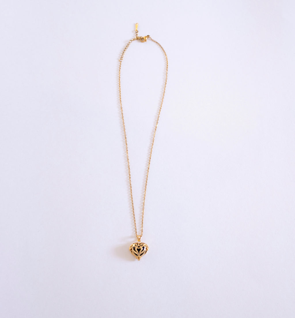 Gold necklace with a heart-shaped pendant on a light purple background