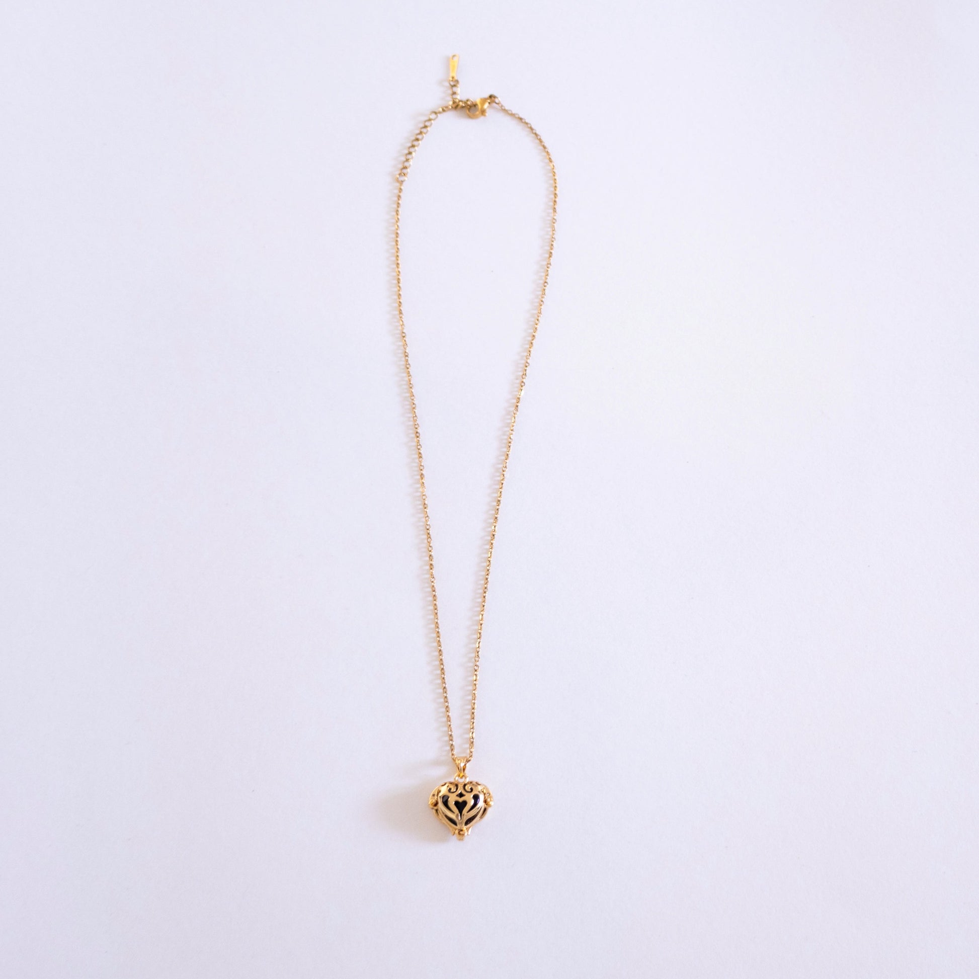 Gold necklace with a heart-shaped pendant on a light purple background