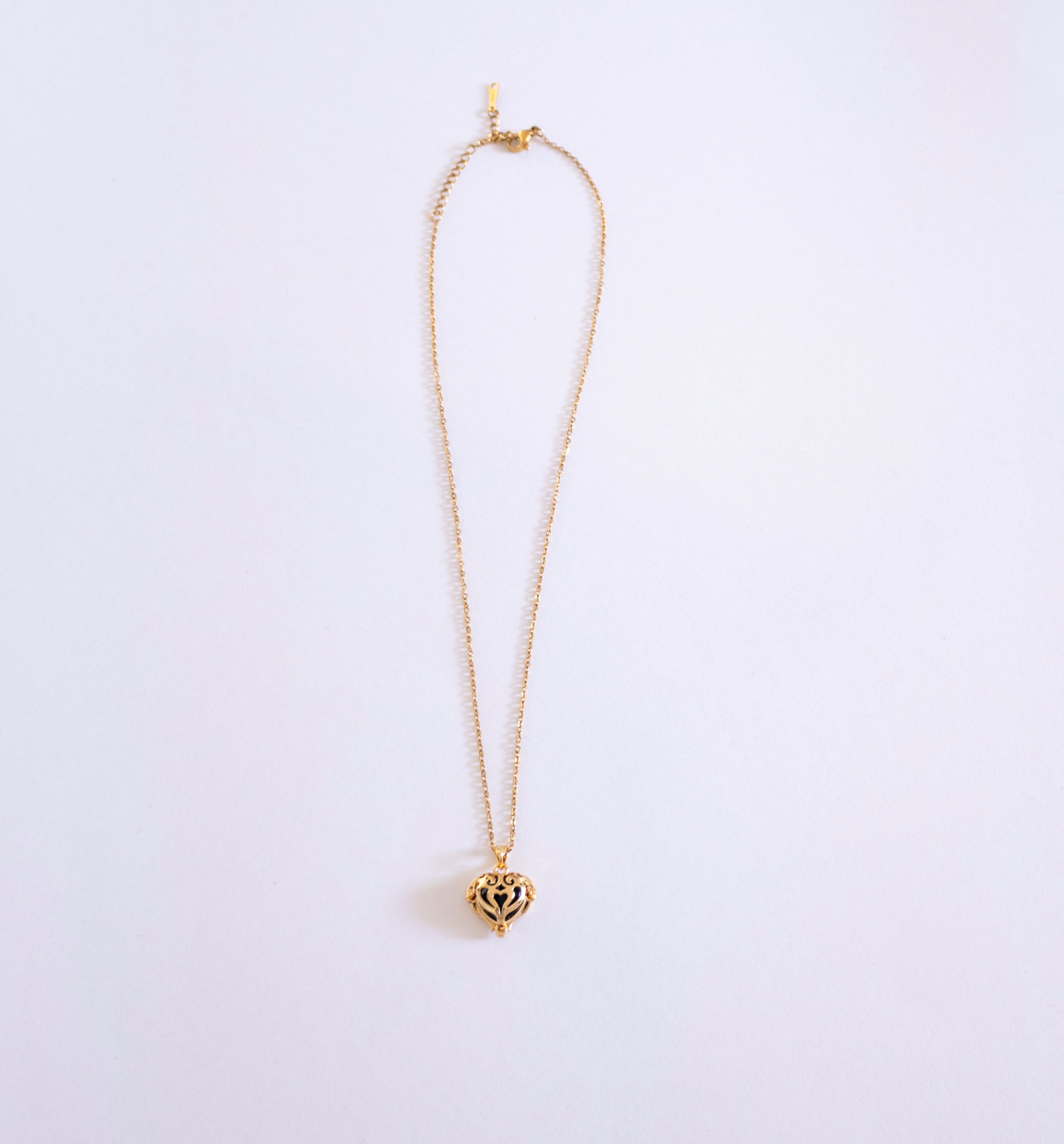 Gold necklace with a heart-shaped pendant on a light purple background